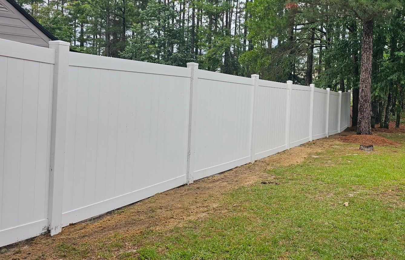 Long white vinyl privacy fence along a grassy yard with trees in the background