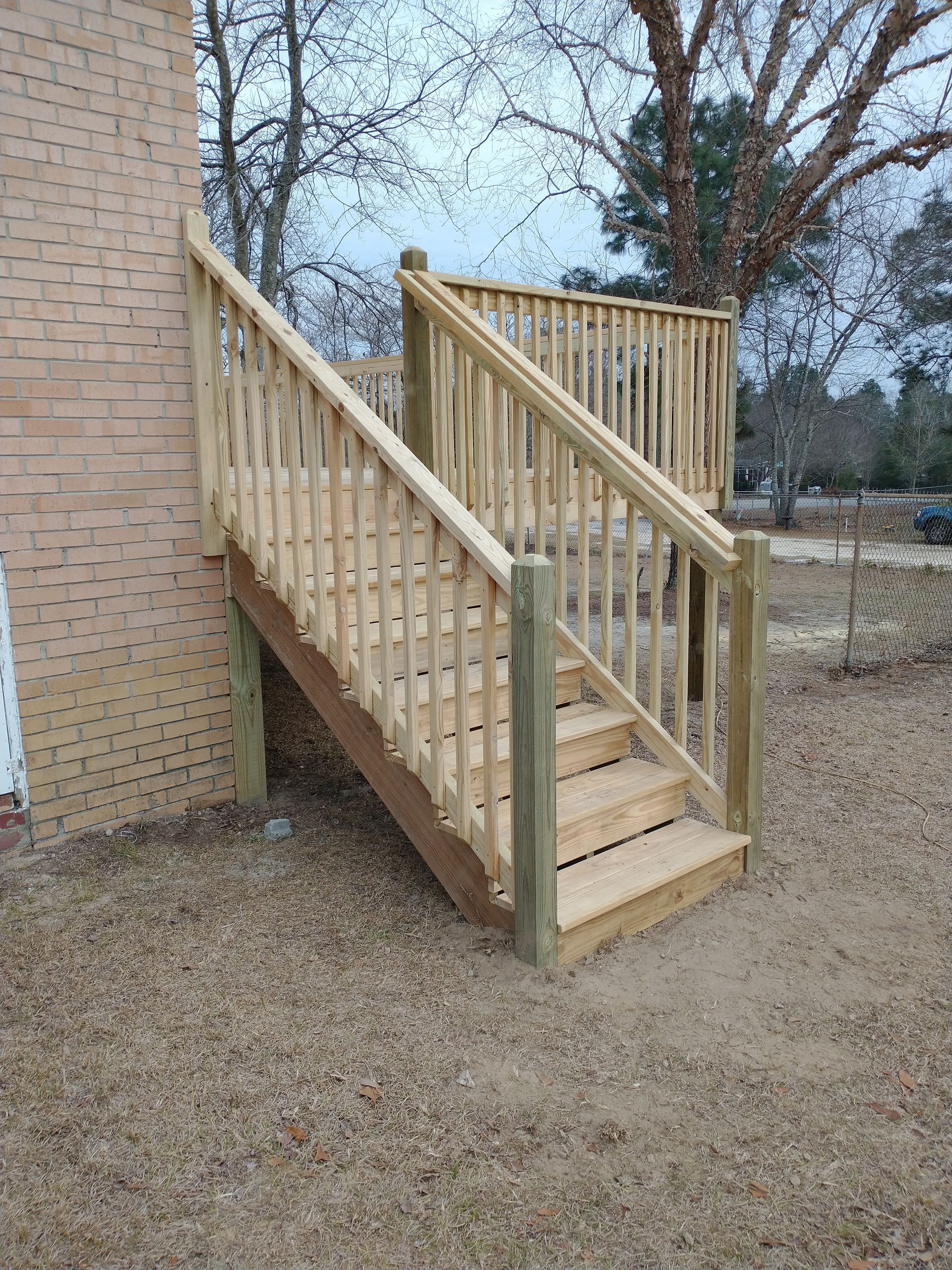 A wooden deck with stairs leading up to it is in front of a brick building.