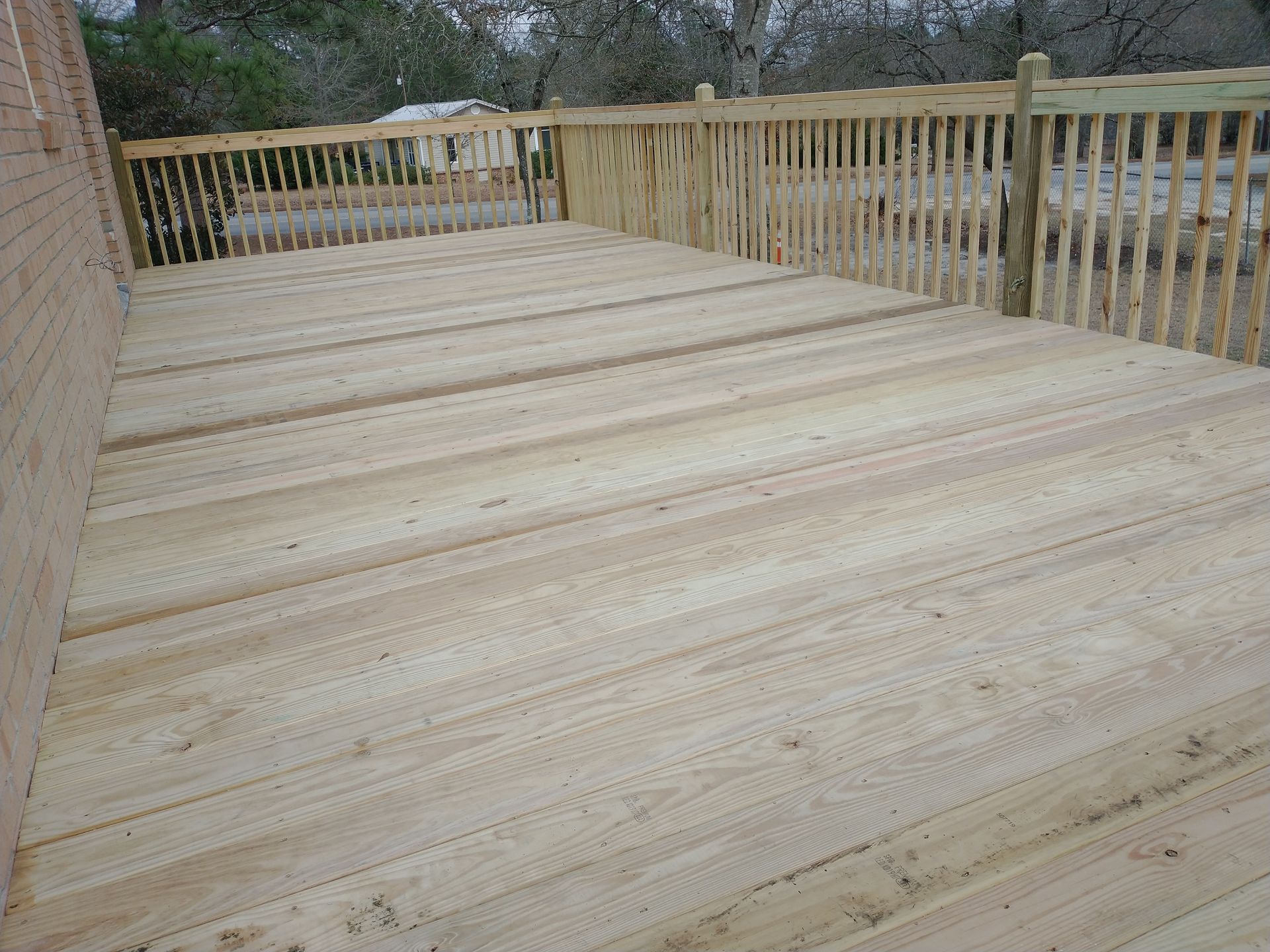 A wooden deck with a wooden railing and a brick building in the background.