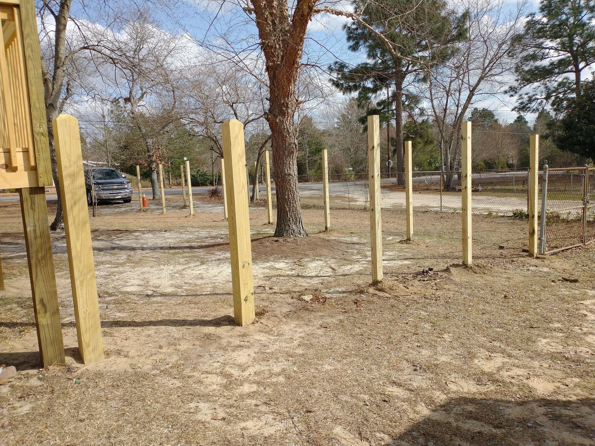 A wooden fence is being built in a dirt field with trees in the background.