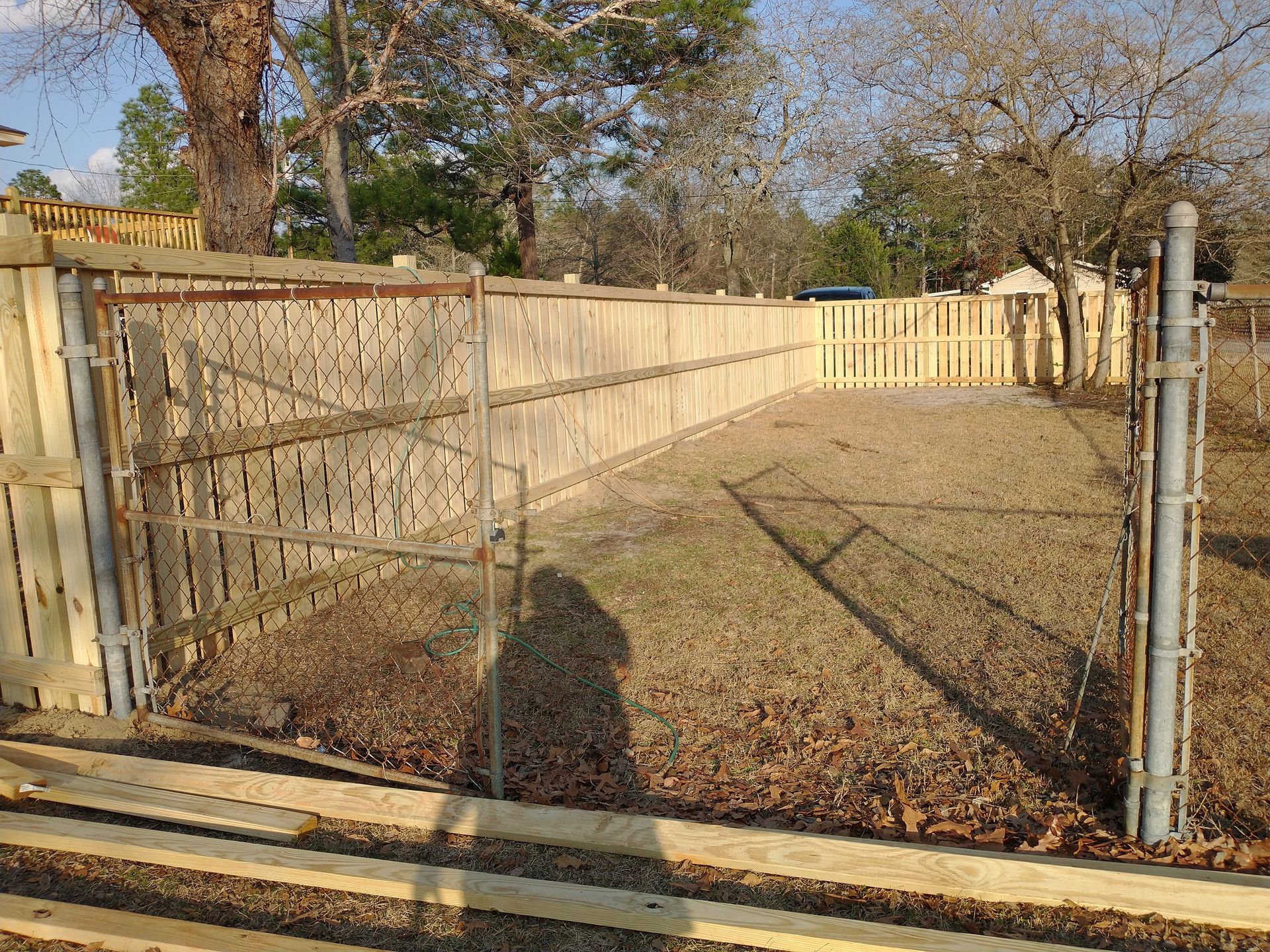 A wooden fence with a metal gate in the middle of a yard.