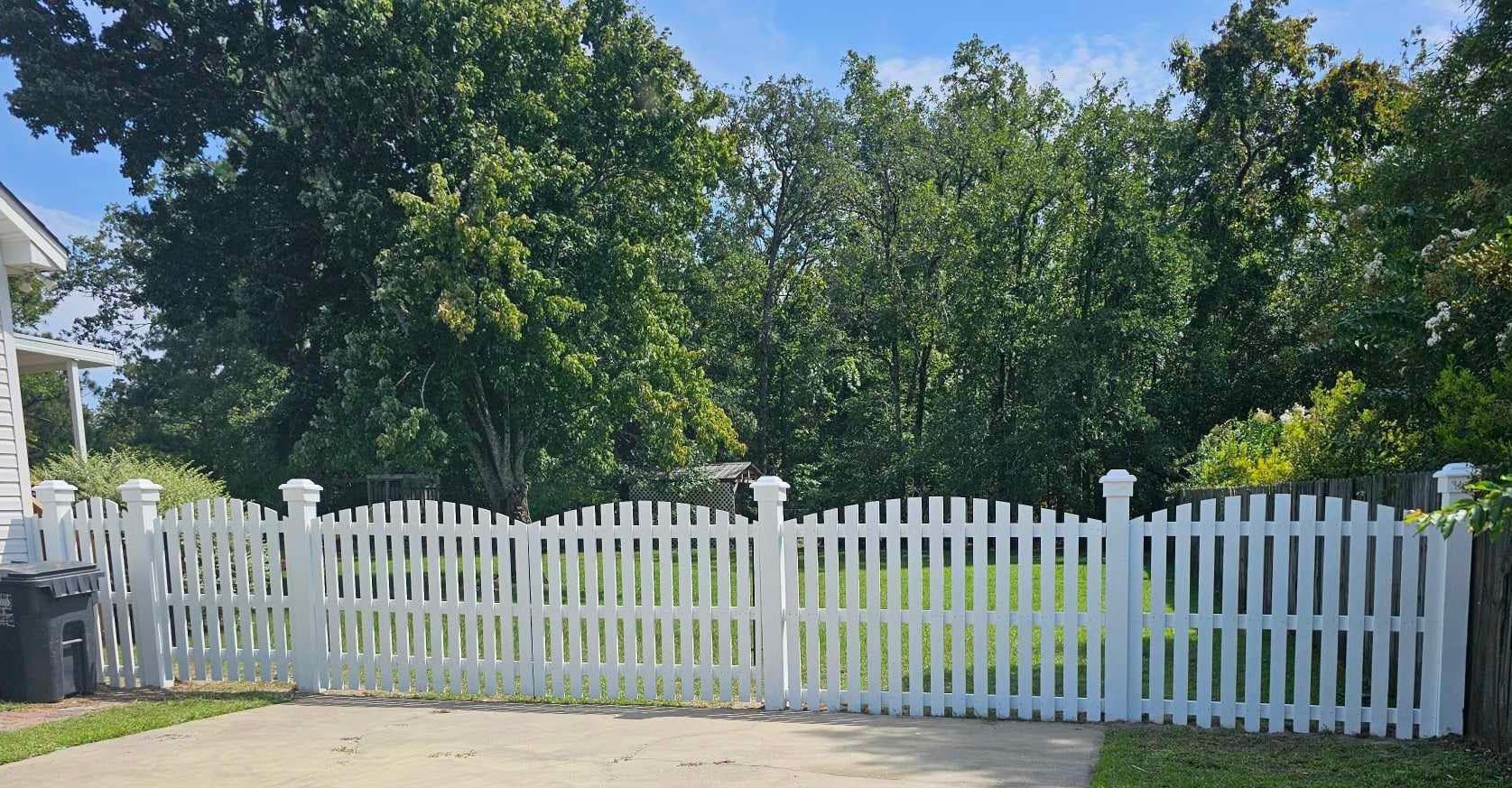 A white picket fence surrounds a driveway in front of a house.