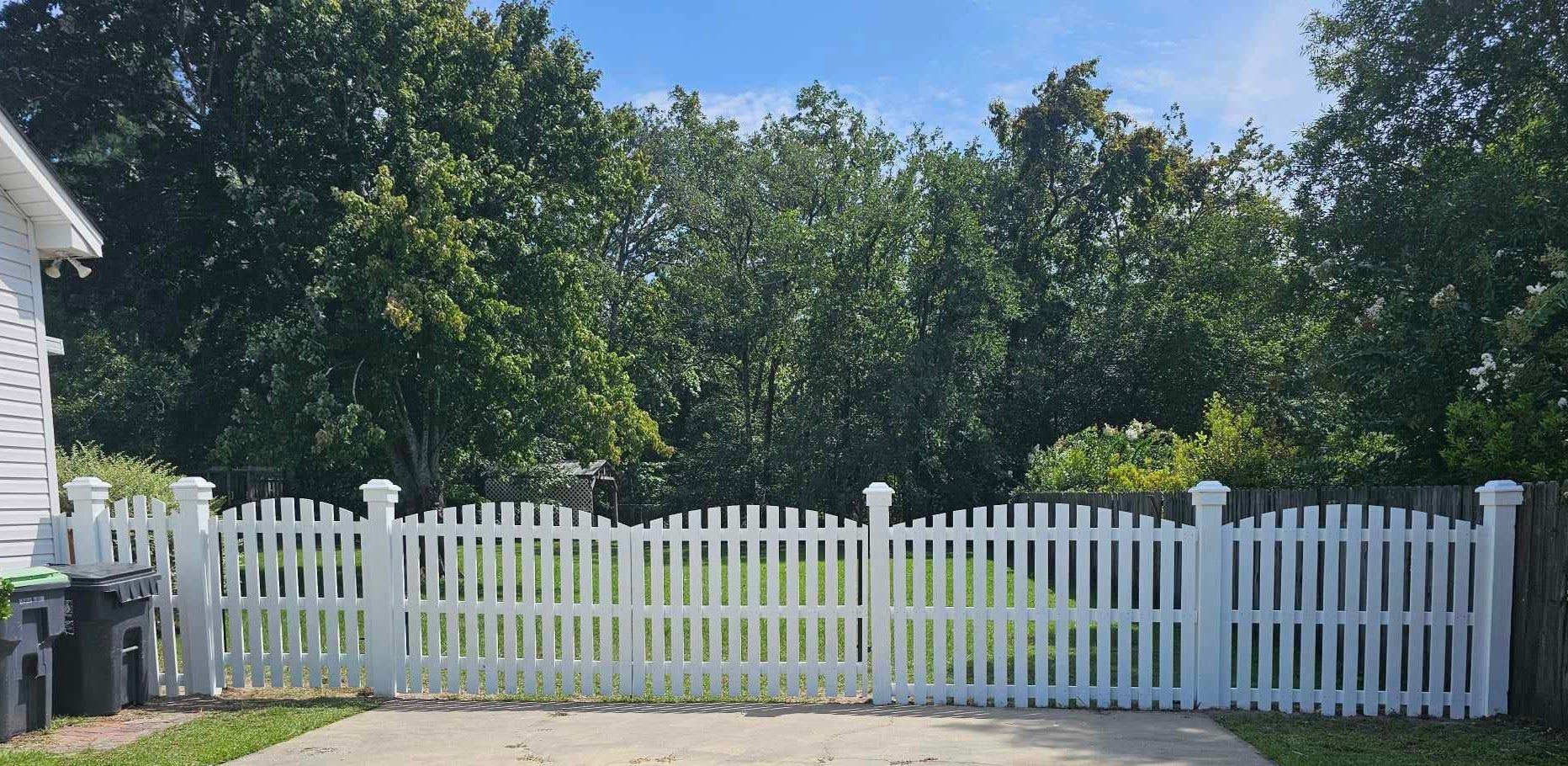 A white picket fence surrounds a driveway in front of a house.