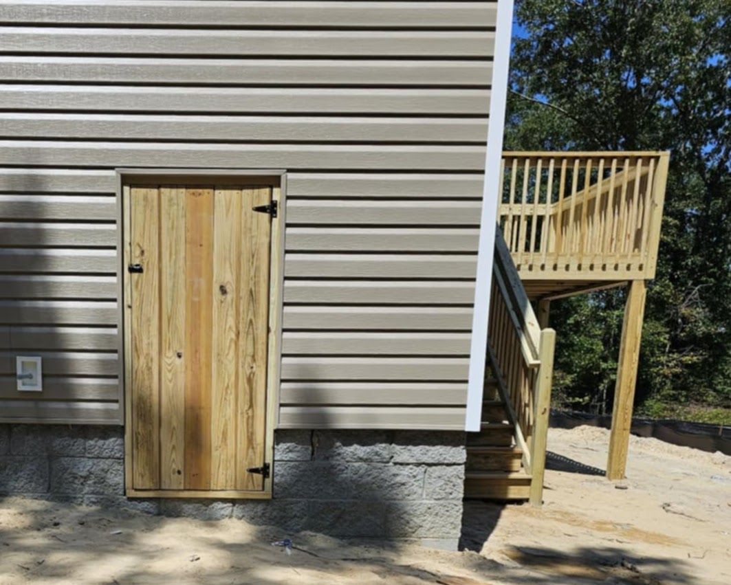 A wooden door is on the side of a house next to a deck.