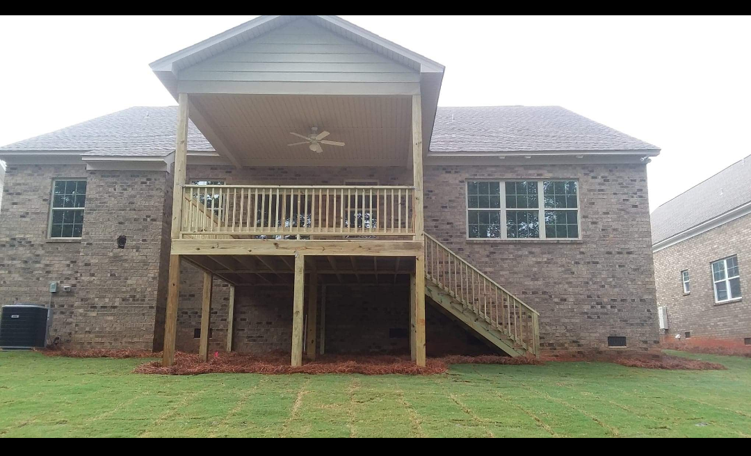 The back of a brick house with a wooden deck and stairs.