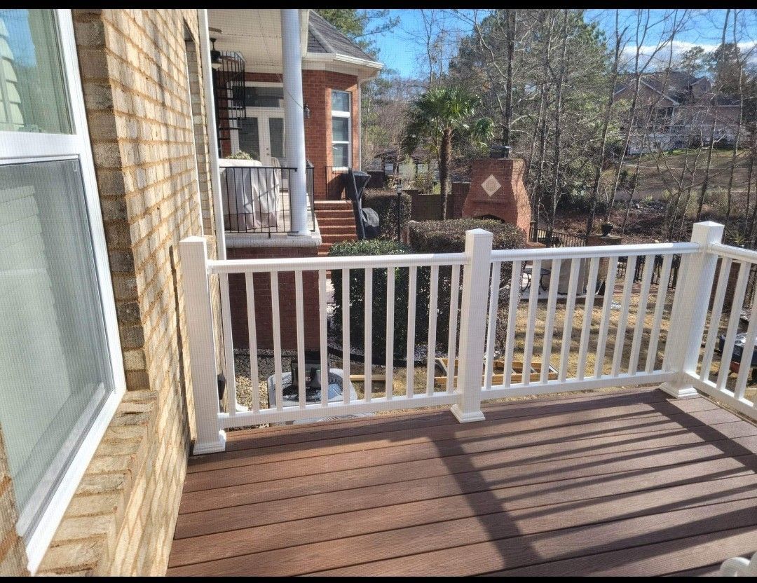 A deck with a white railing and a brick building in the background.