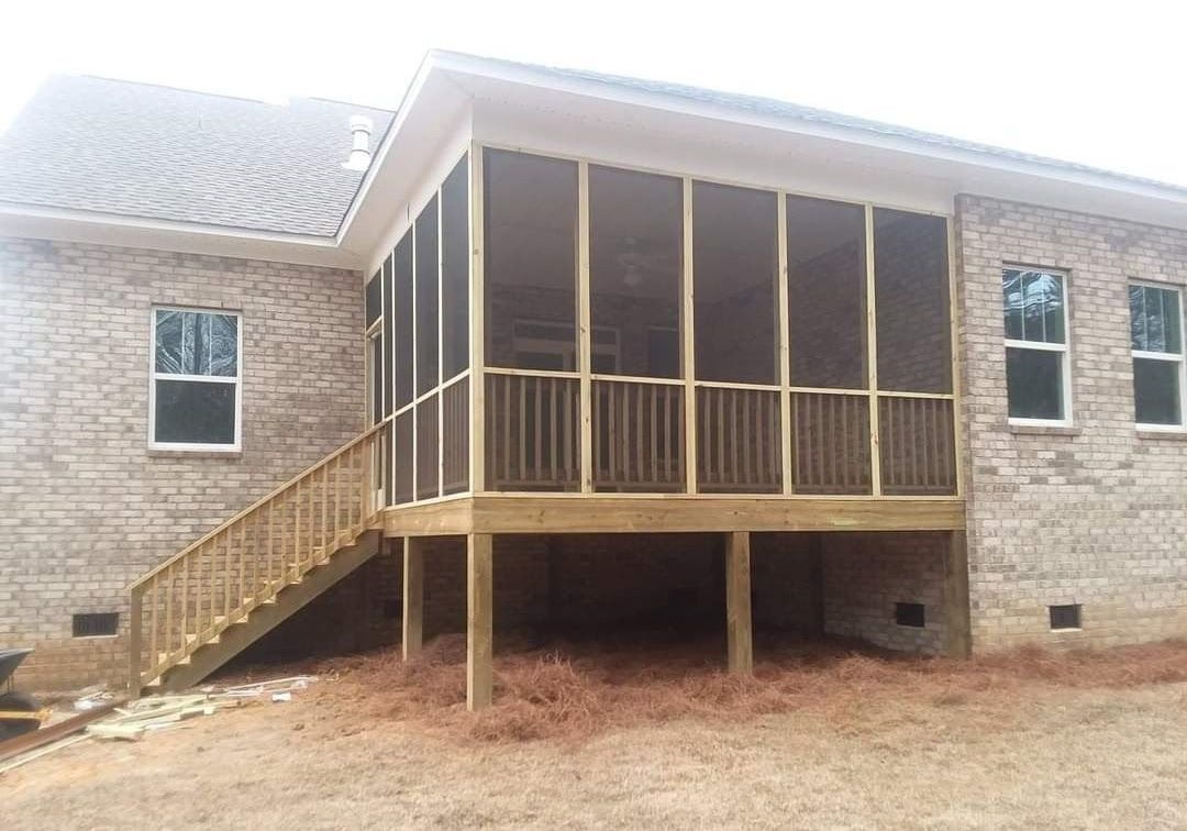 A screened in porch with stairs and a brick house in the background.