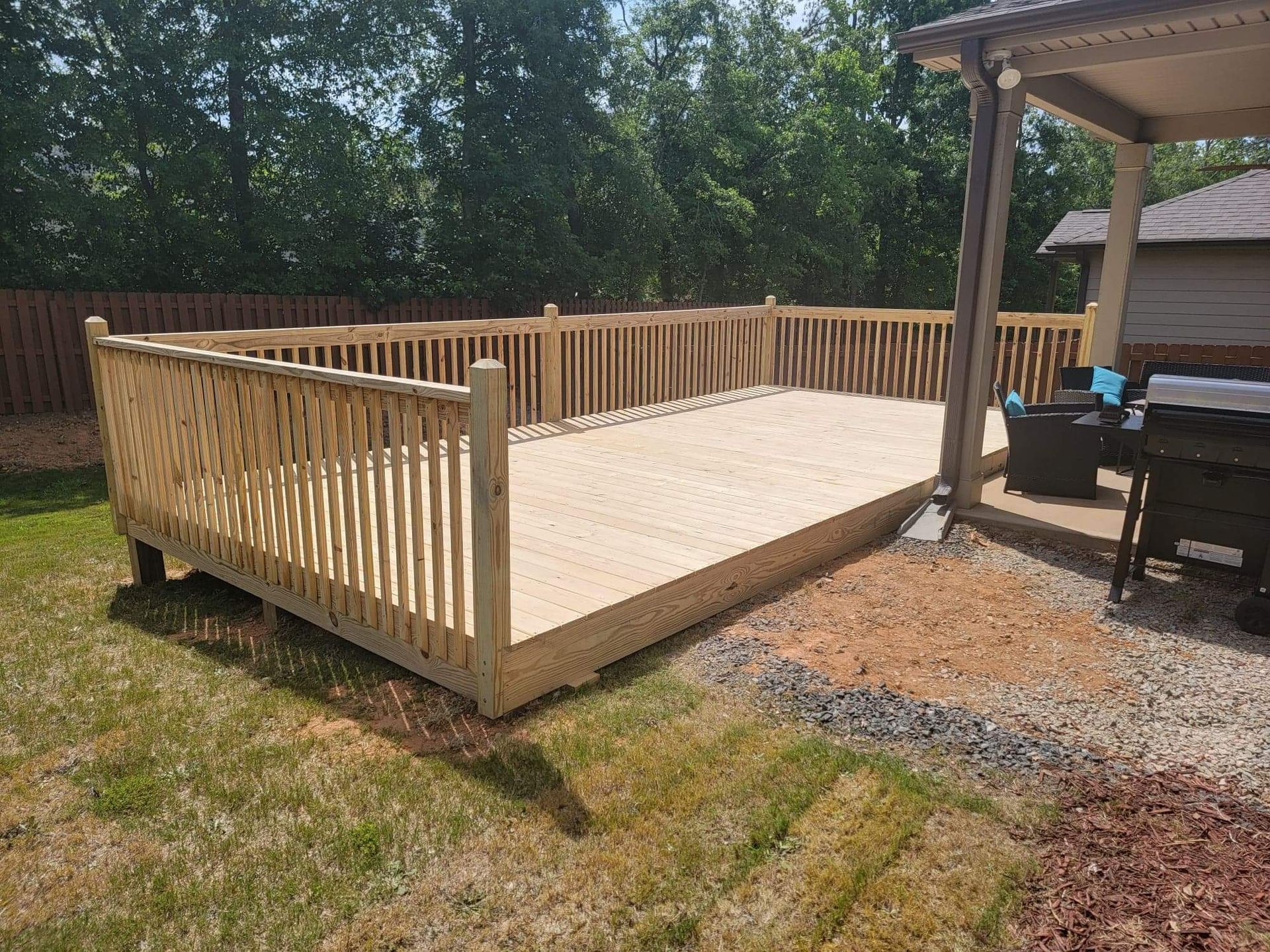 A large wooden deck with a railing in the backyard of a house.