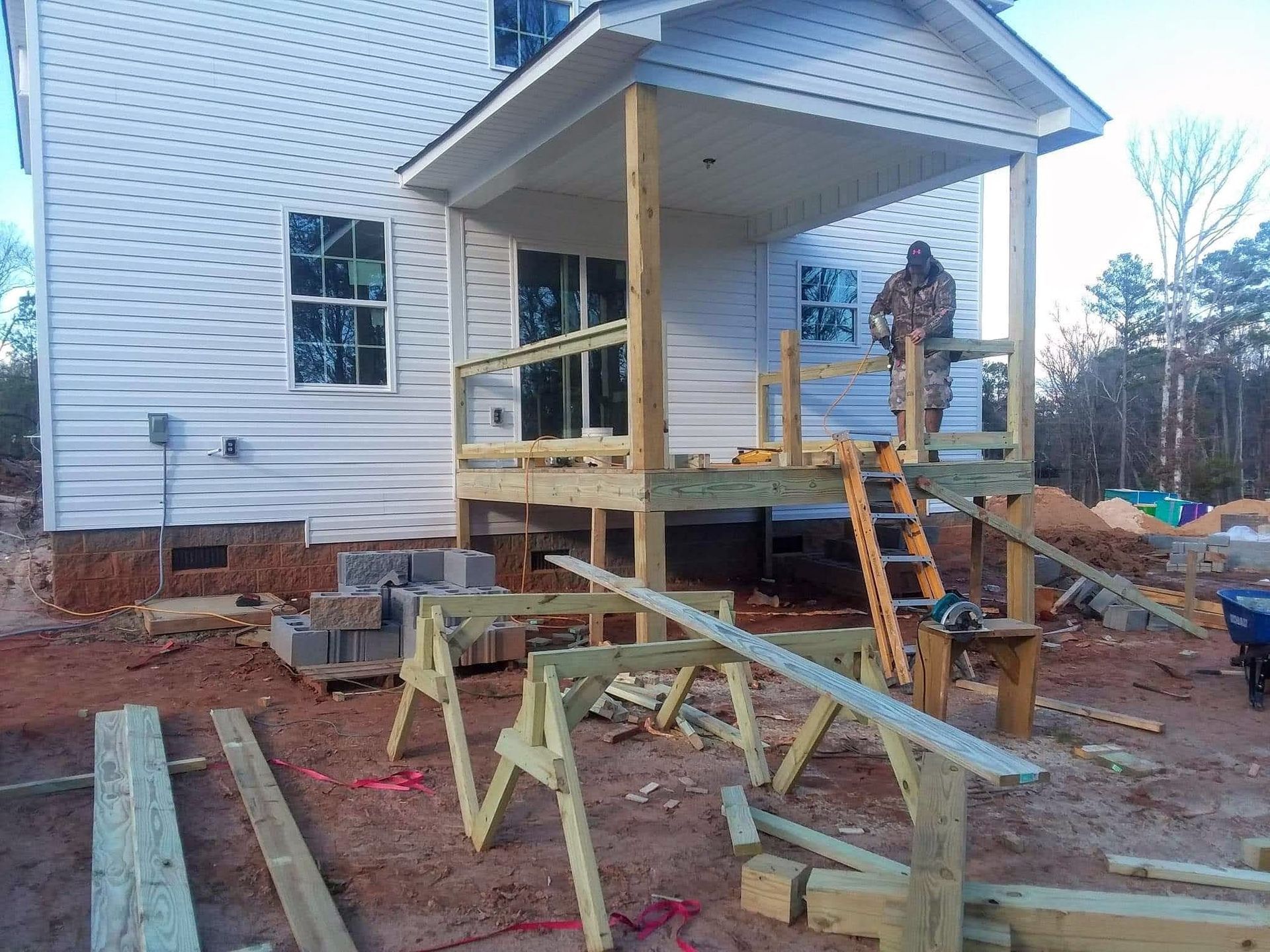 A man is standing on a wooden porch in front of a white house.