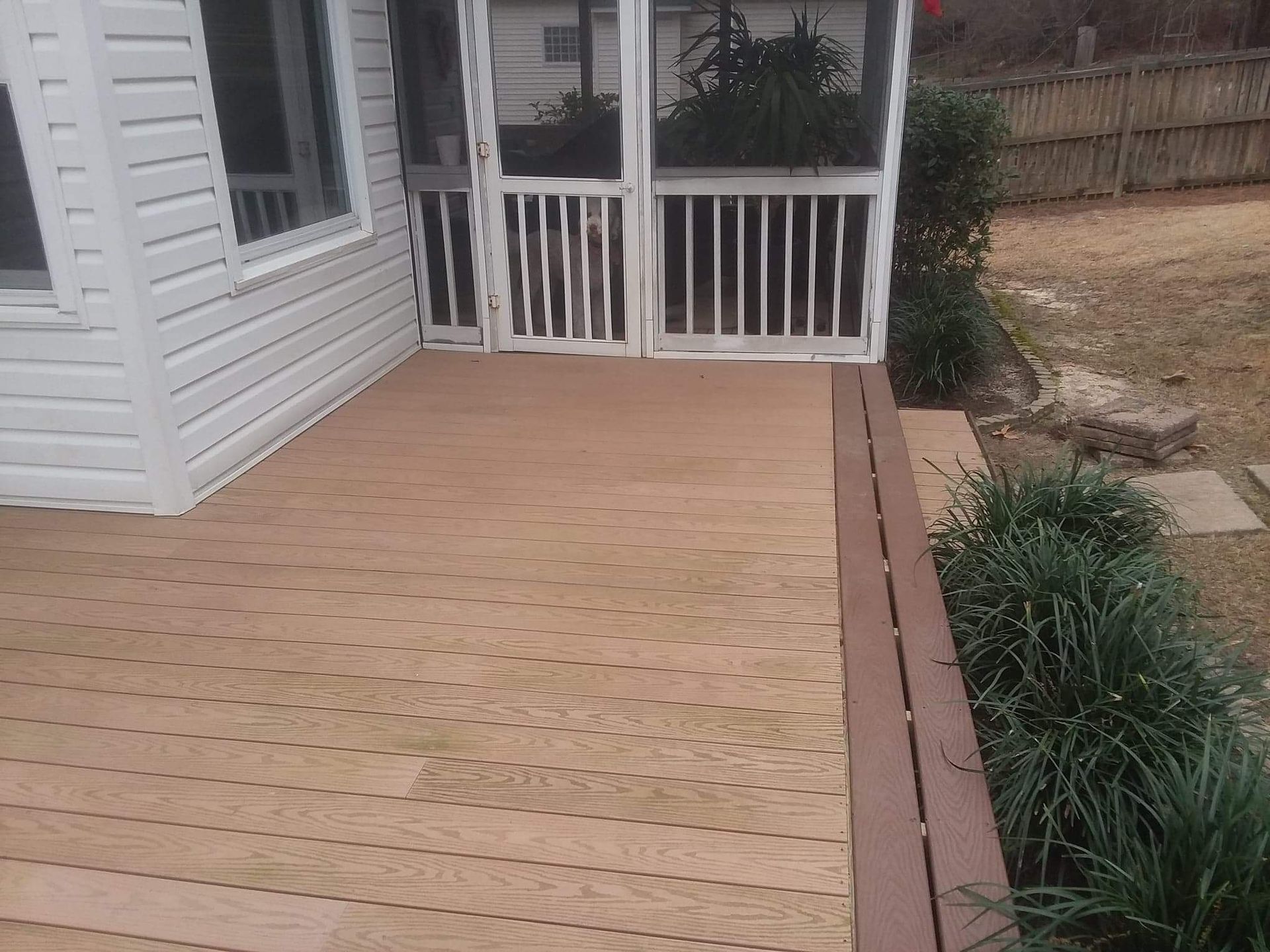A screened in porch with a wooden deck and a white house in the background.