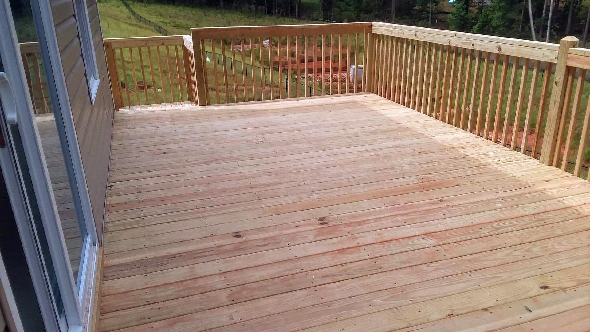 A wooden deck with a wooden railing and a sliding glass door.