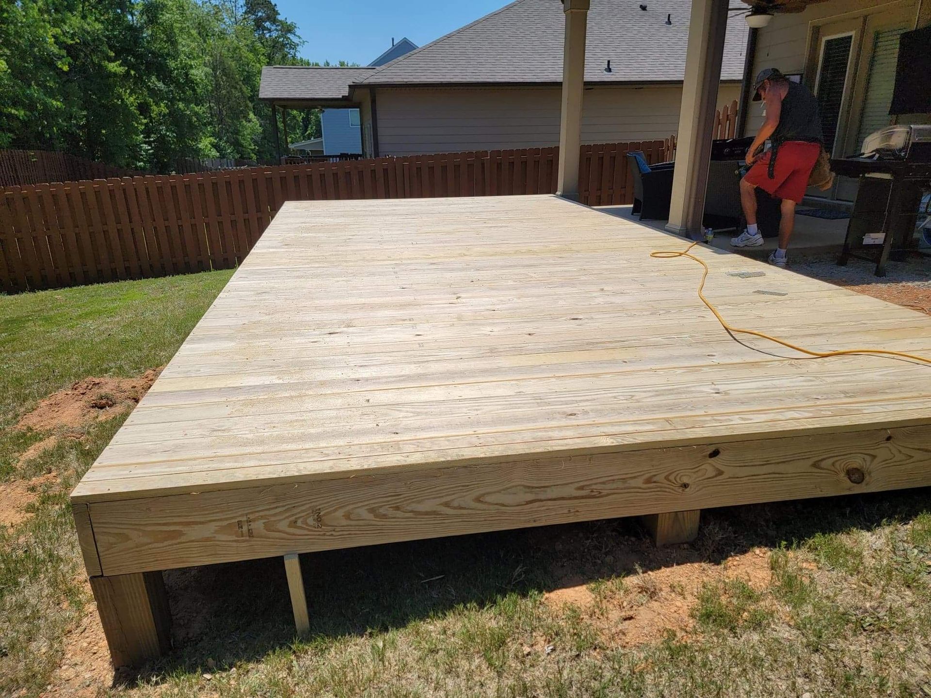 A man is standing on a wooden deck in a backyard.