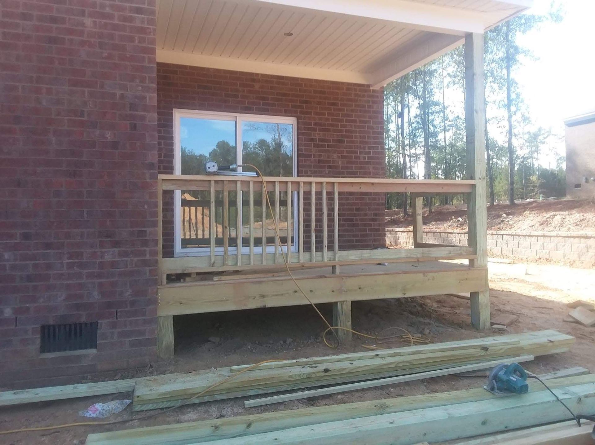 A wooden deck is being built in front of a brick house.