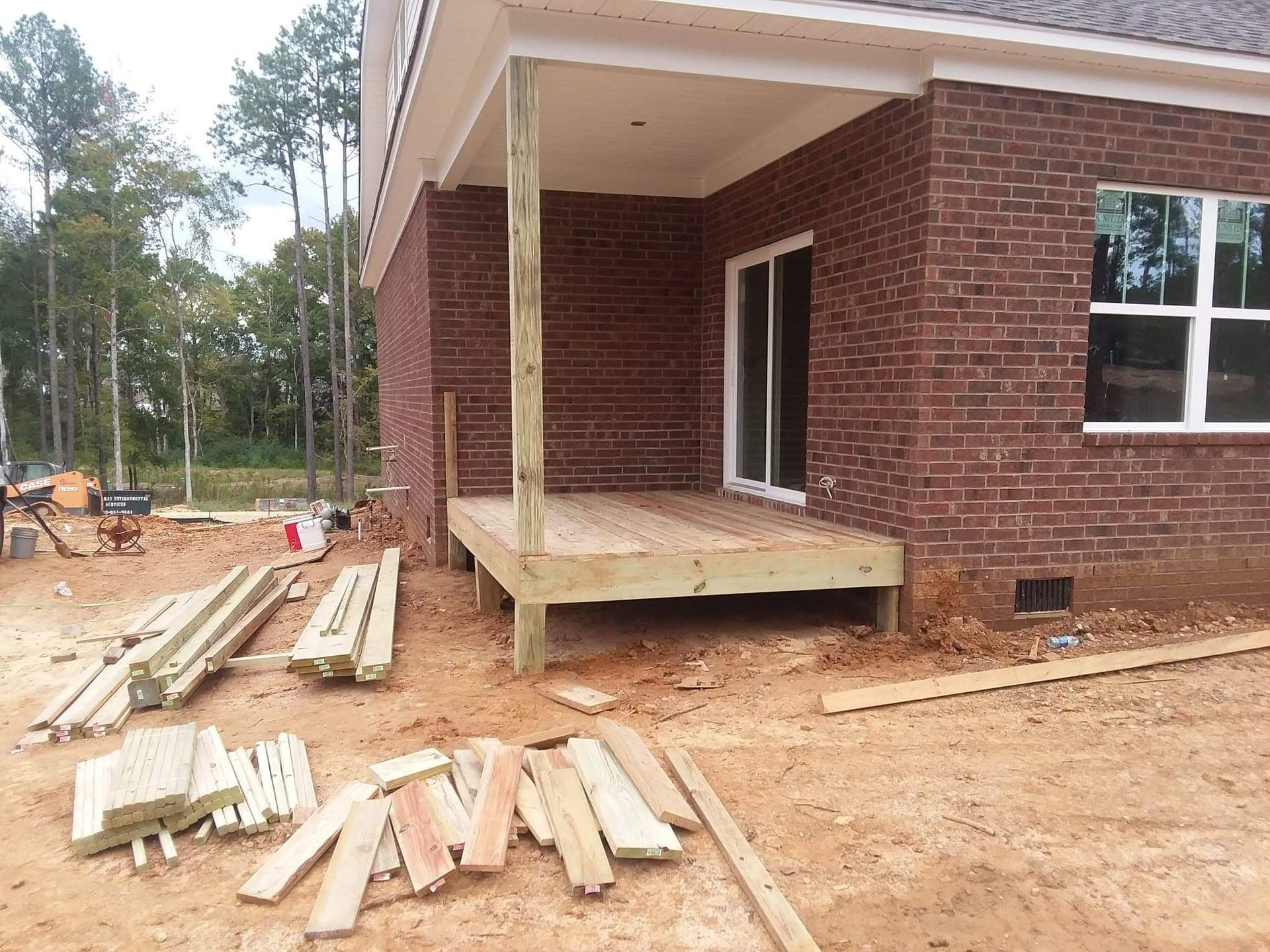 A wooden deck is being built in front of a brick house.