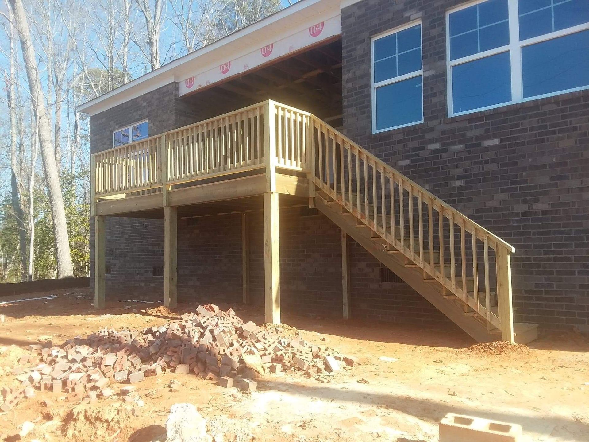 A wooden deck with stairs leading up to it is in front of a brick building.