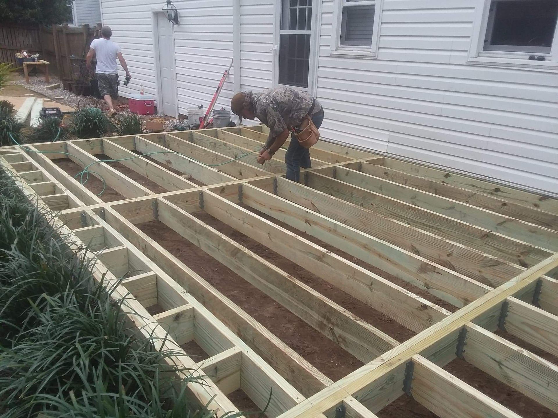 A man is working on a wooden deck in front of a white house