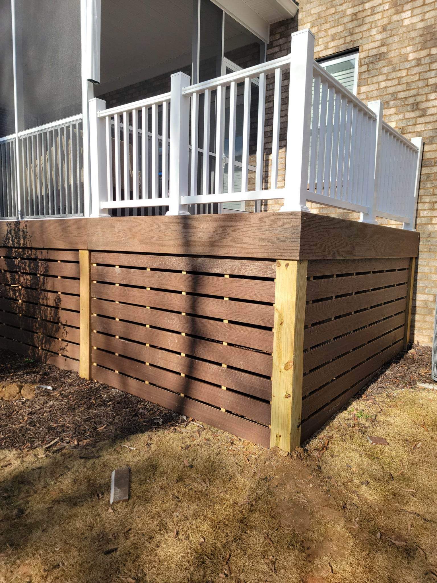 A wooden deck with a white railing and a screened in porch.