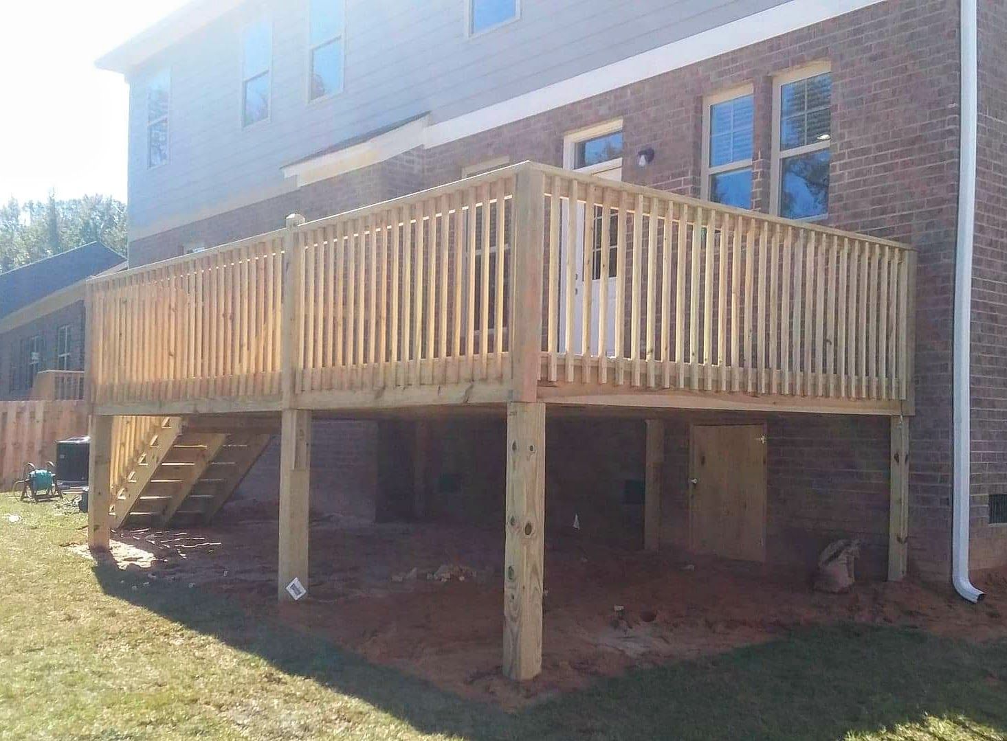 A wooden deck with stairs is in the backyard of a brick house.