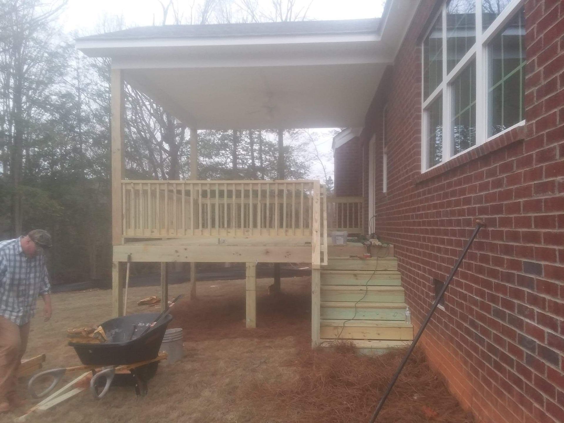 A man is working on a wooden deck in front of a brick house.