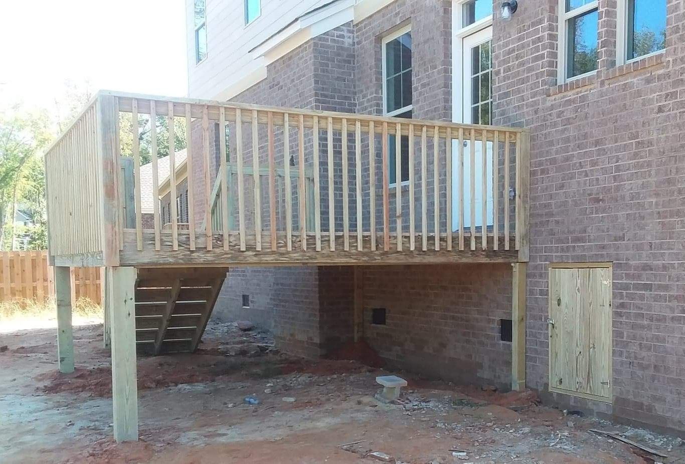 A wooden deck is being built in the backyard of a brick house.