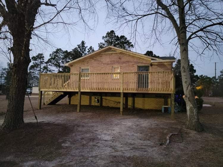 A brick house with a wooden deck is surrounded by trees