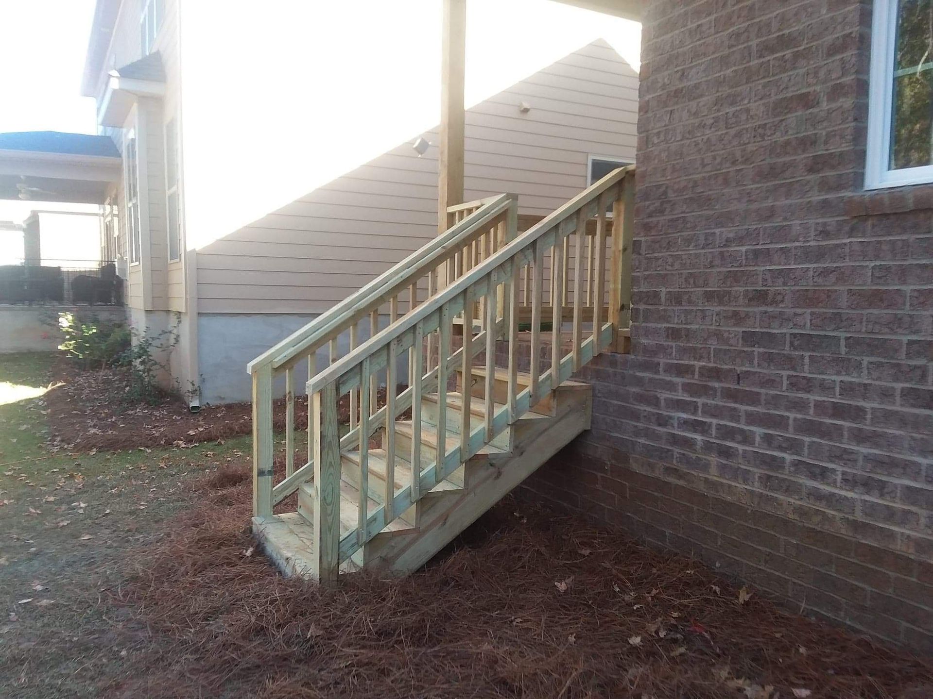 A wooden deck with stairs leading up to a brick house.