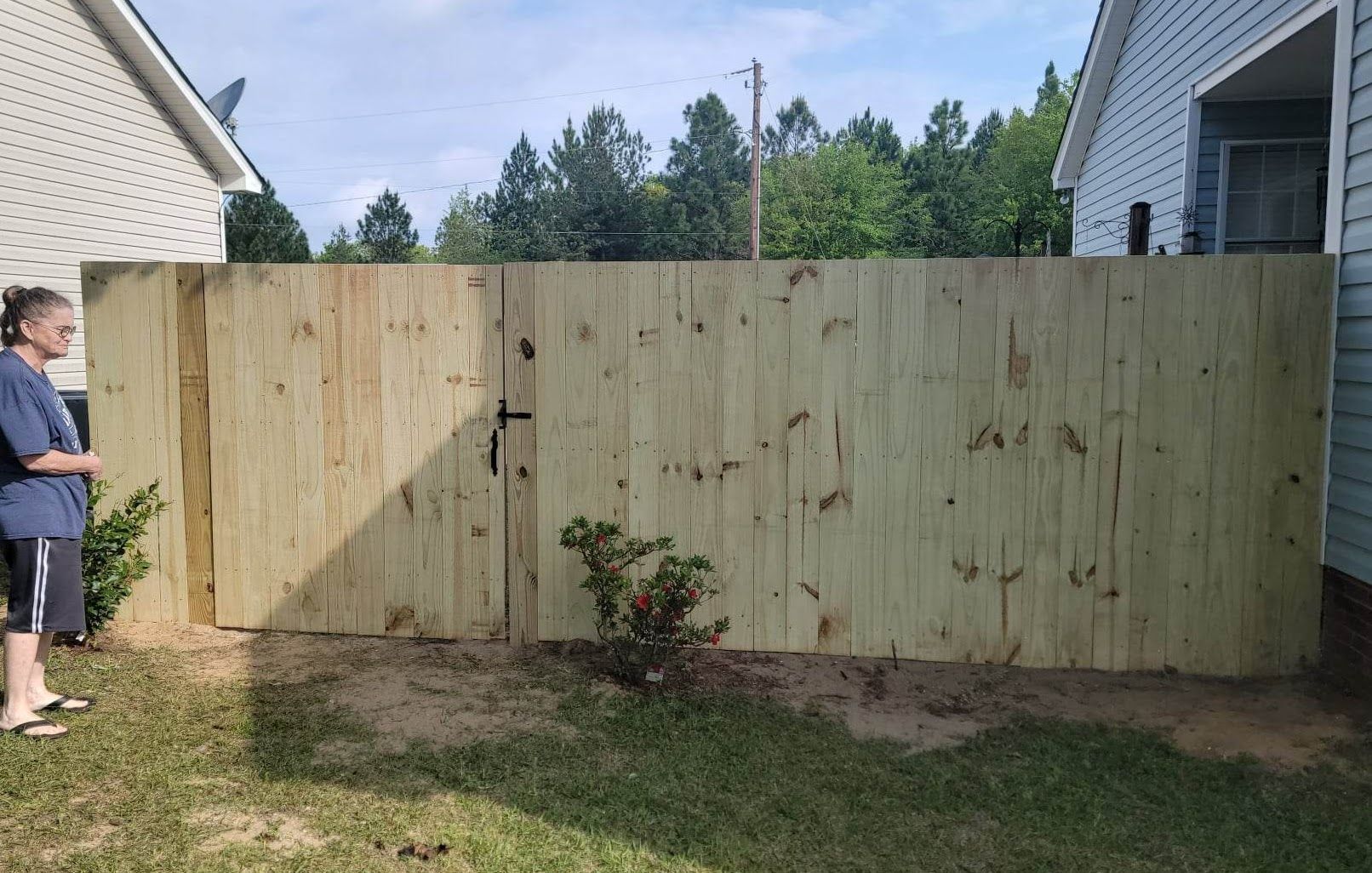 A woman is standing next to a wooden fence in front of a house.