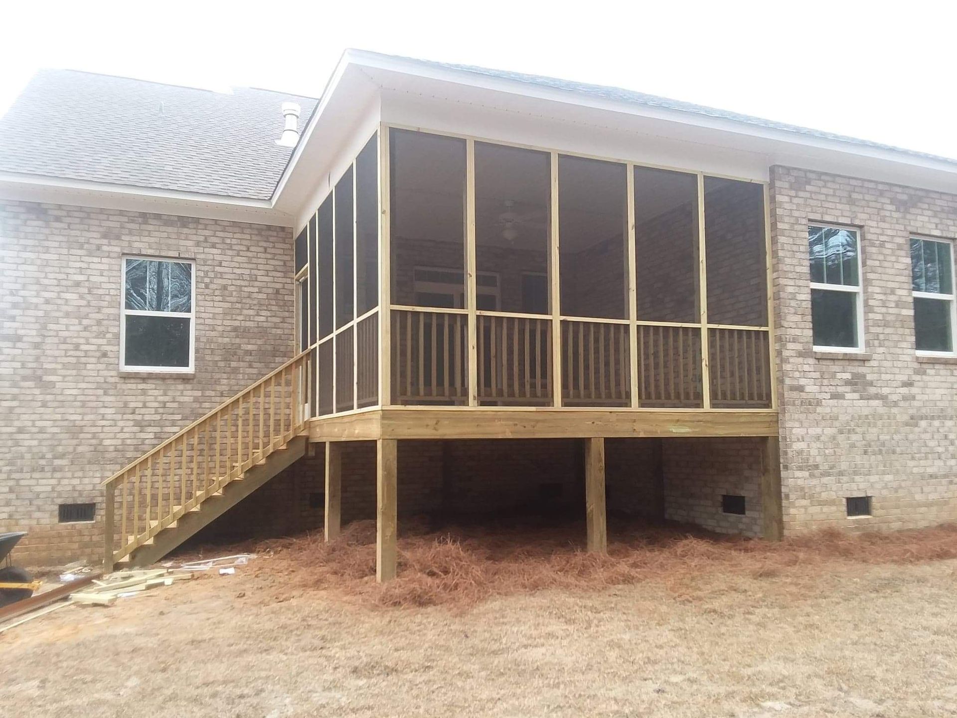 A screened in porch with stairs on the side of a brick house.