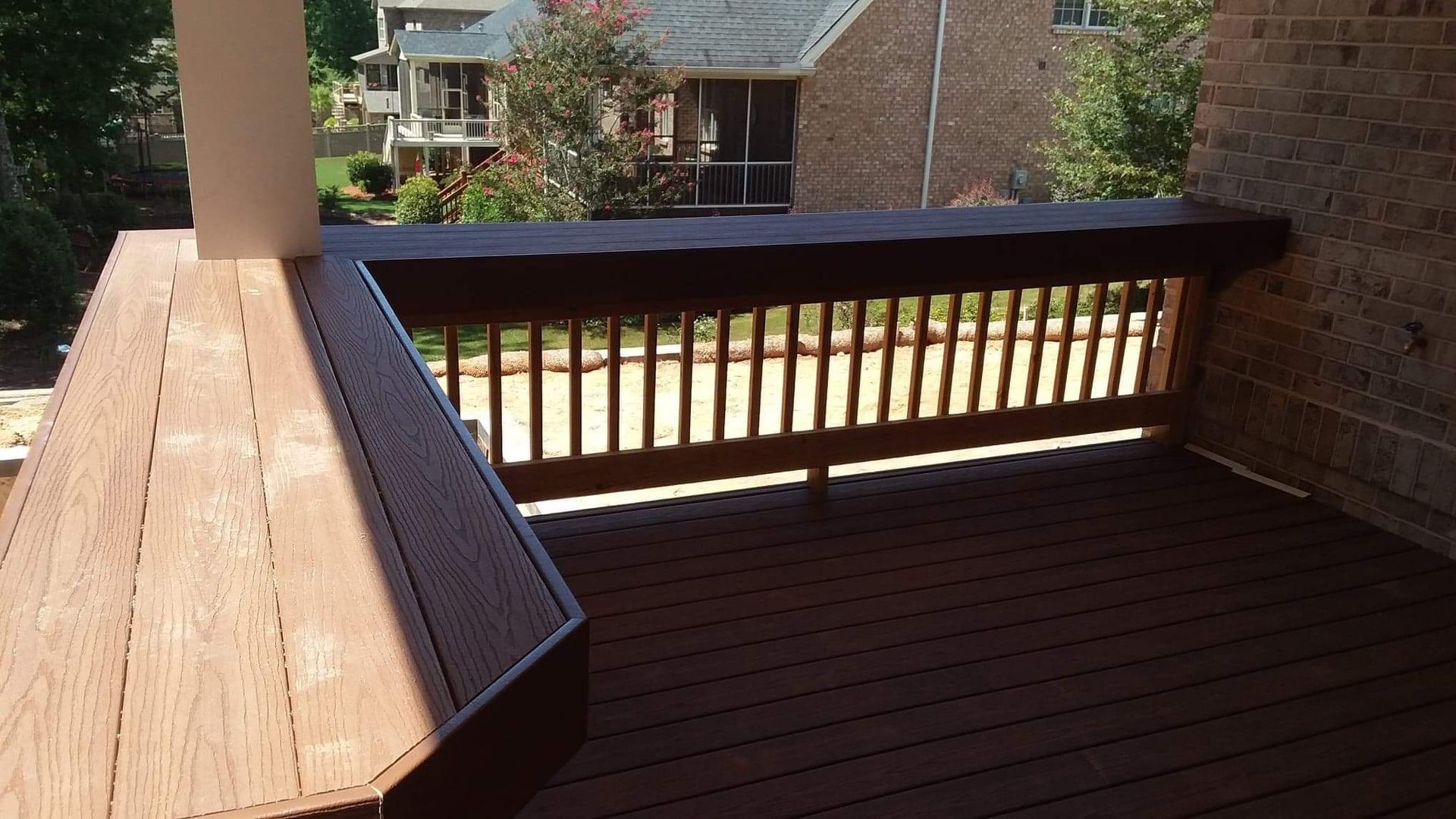 A wooden deck with a brick house in the background