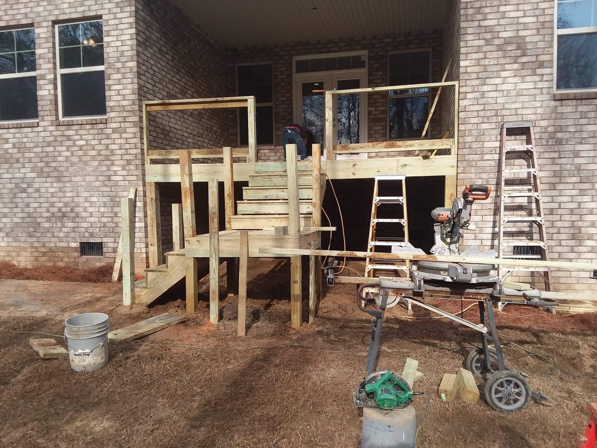 A wooden deck is being built in front of a brick house