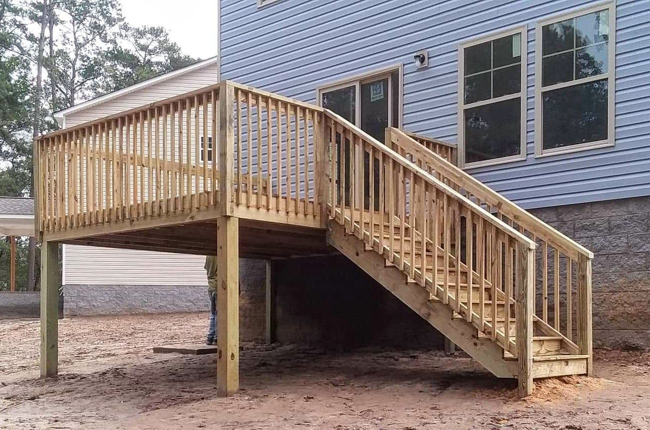 A wooden deck with stairs leading up to the back of a house.