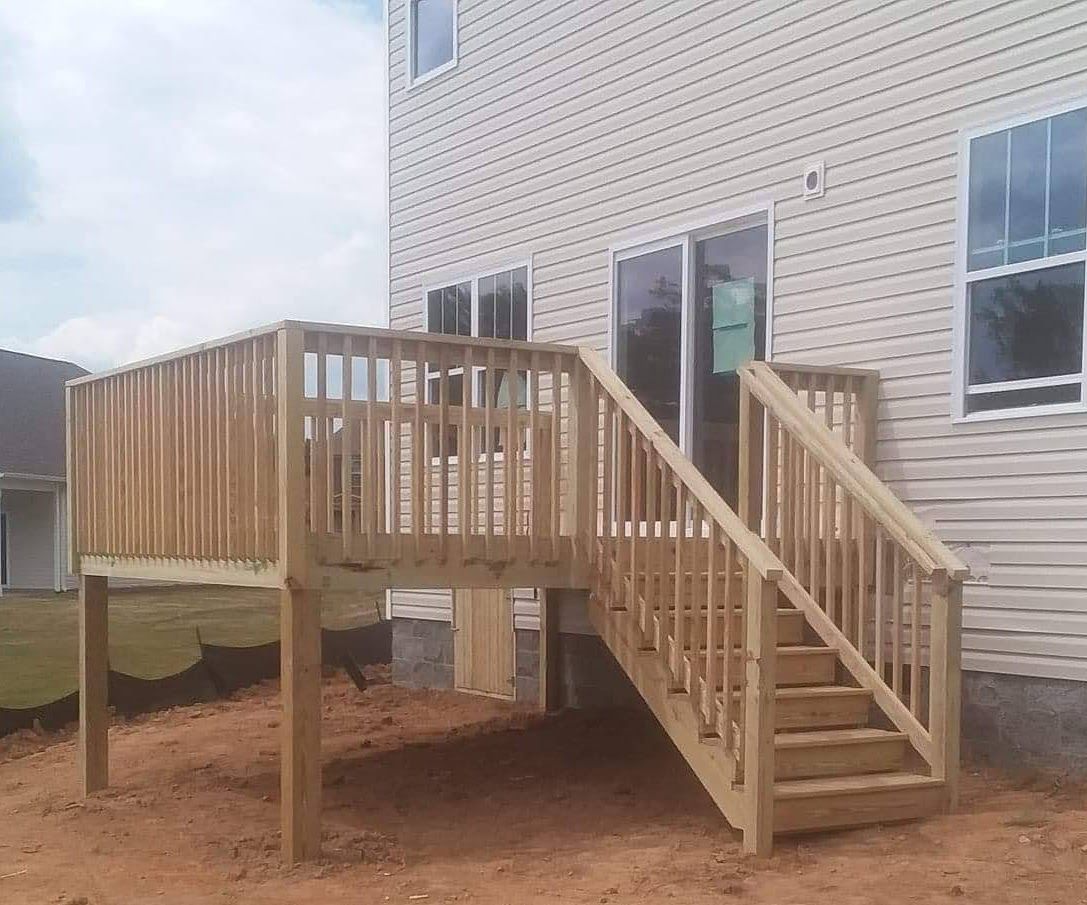 A wooden deck with stairs leading up to it is in front of a house.