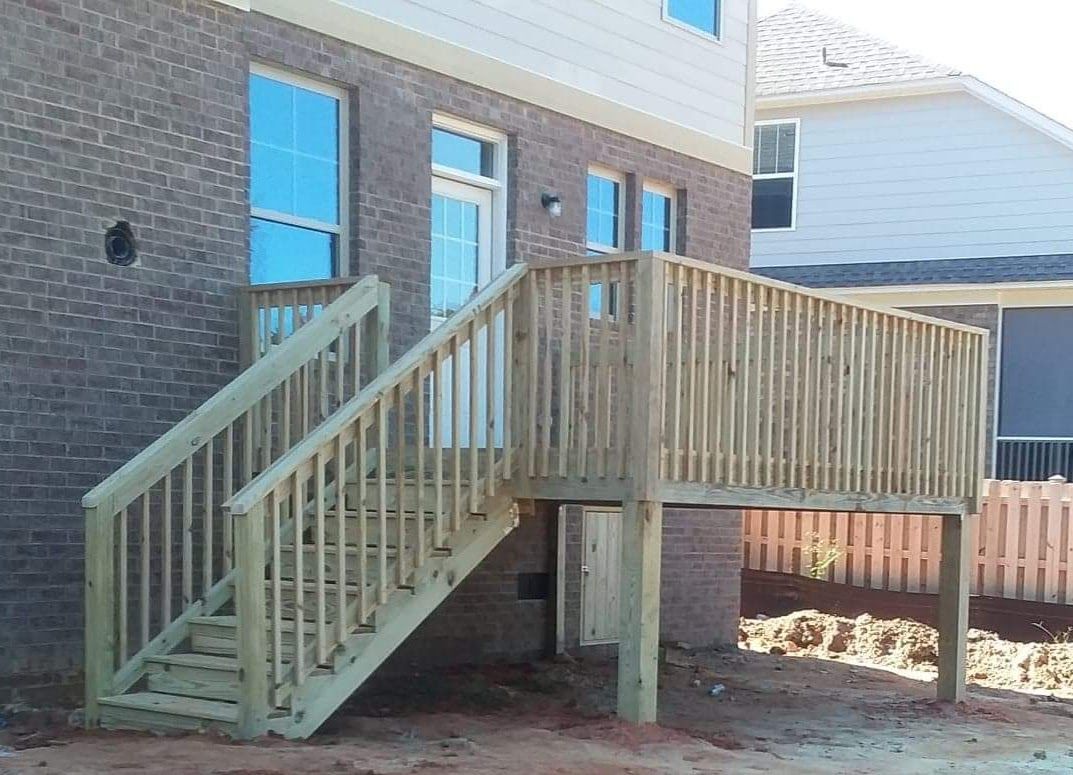 A wooden deck with stairs leading up to it is in front of a brick building.