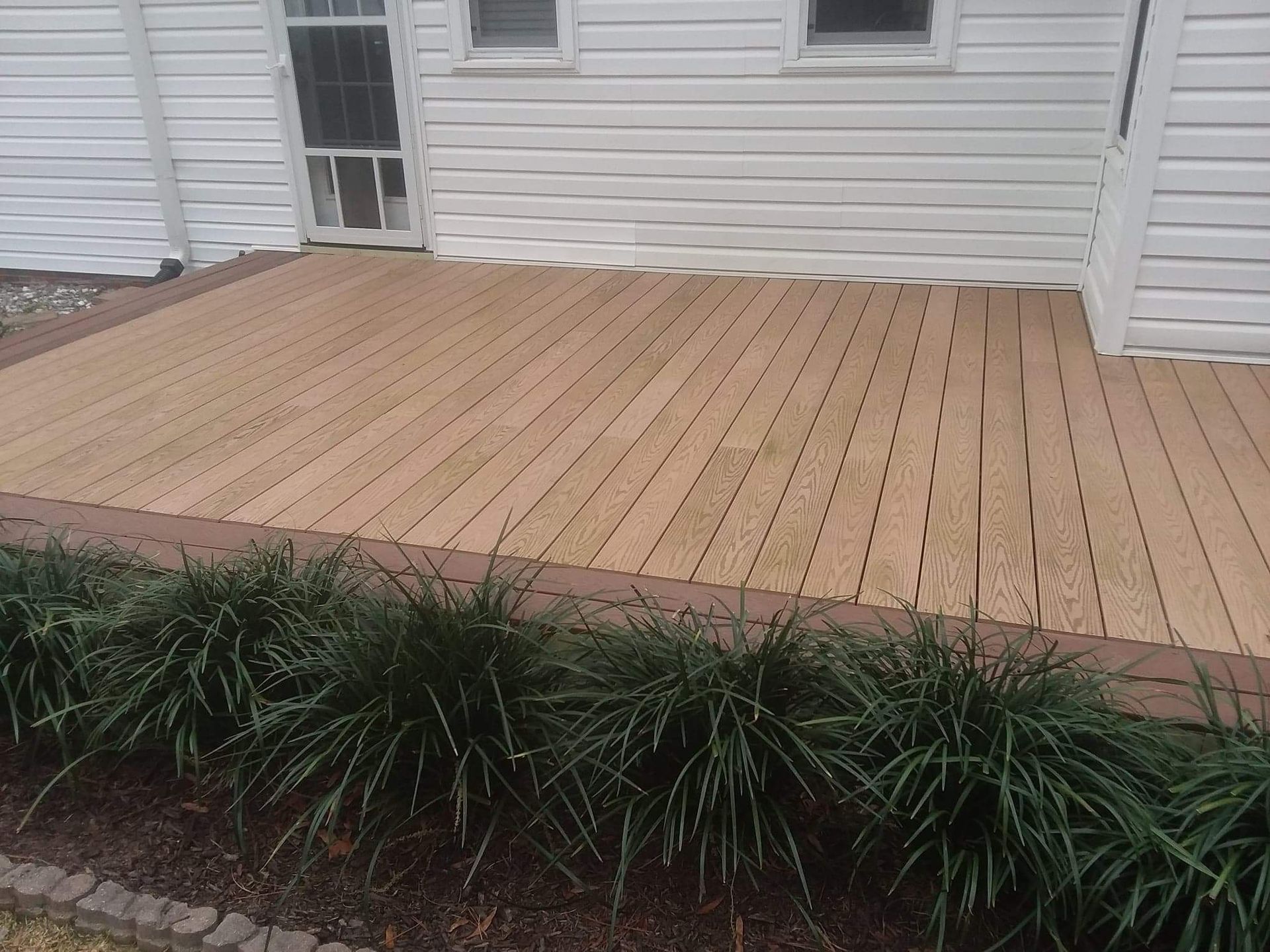 A wooden deck is sitting in front of a white house.