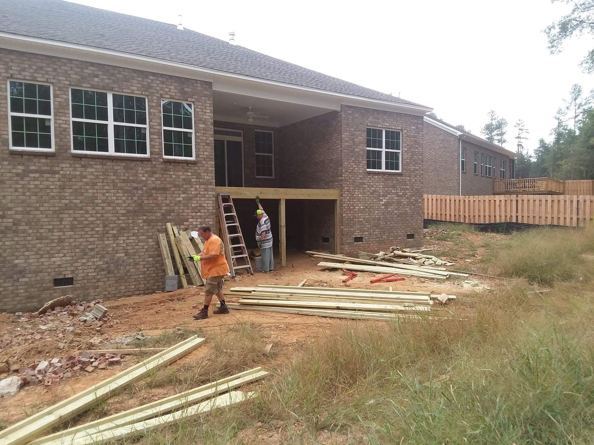 Two men are standing in front of a brick building under construction.