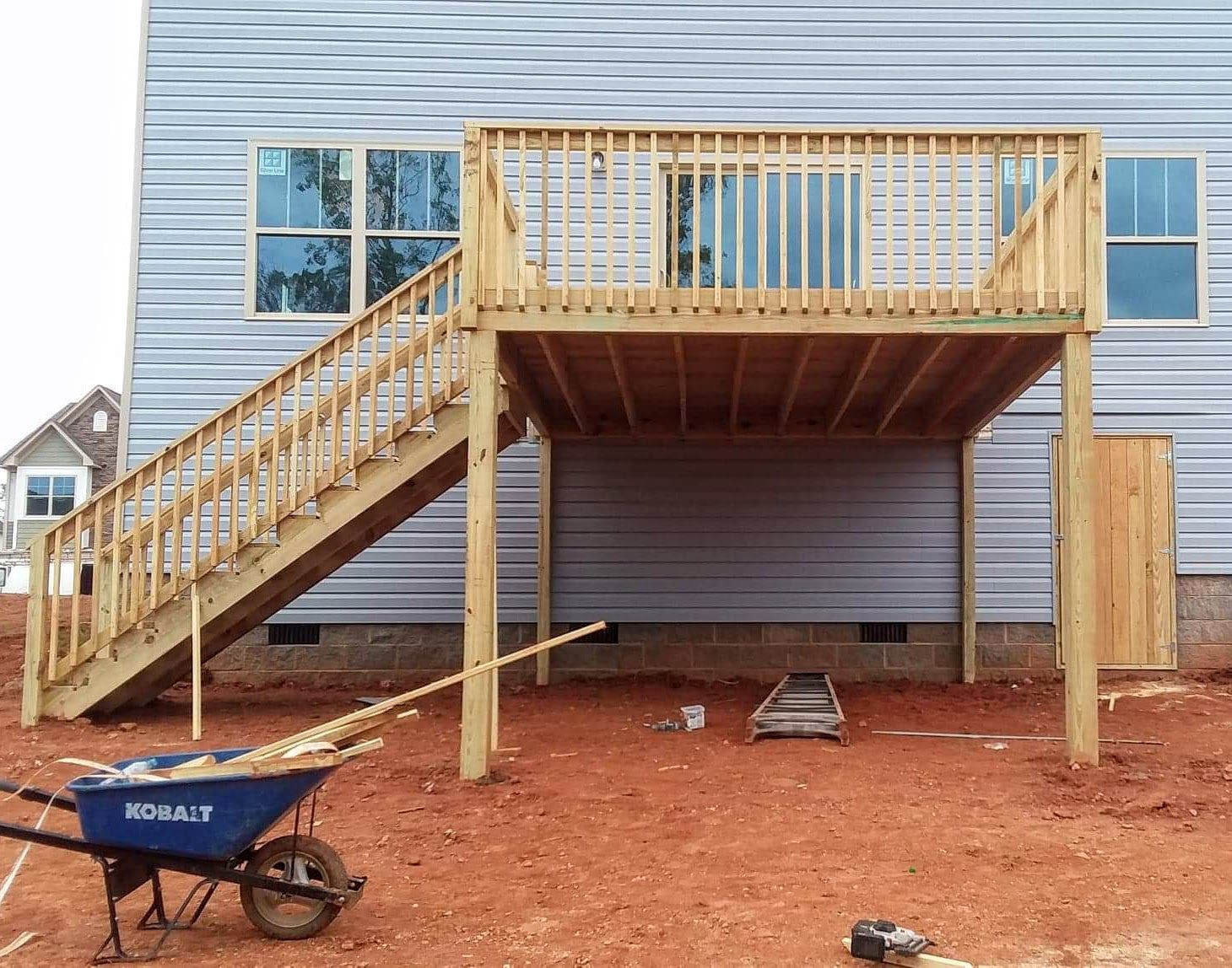 A blue wheelbarrow is parked in front of a house under construction.