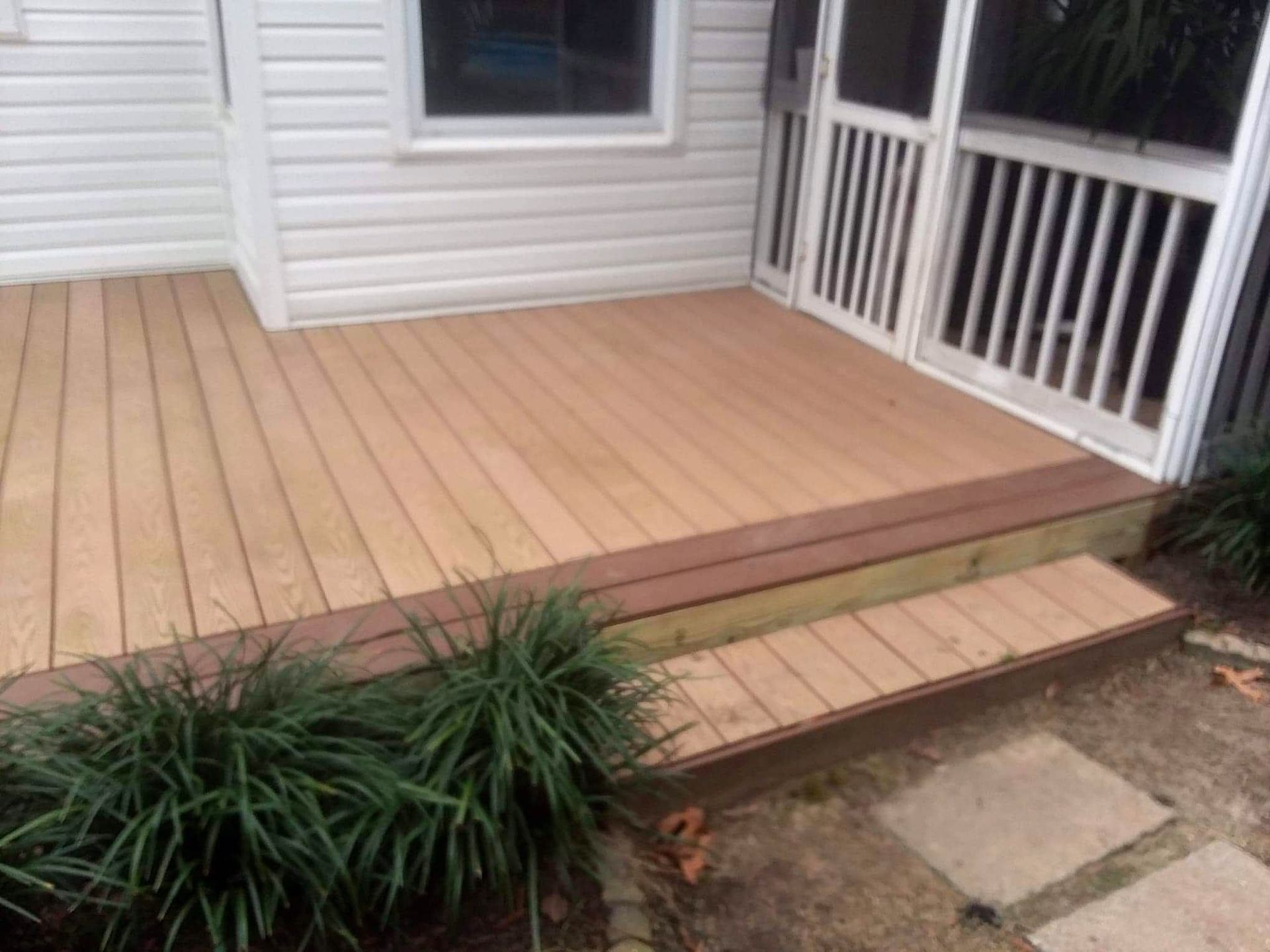 A screened in porch with a wooden deck and steps leading to it.