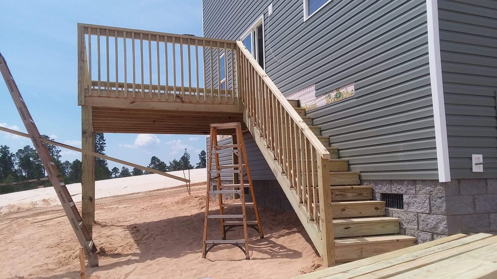 A wooden deck with stairs and a ladder in front of a house