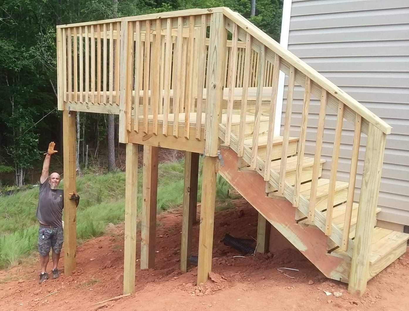 A man is standing next to a wooden deck with stairs
