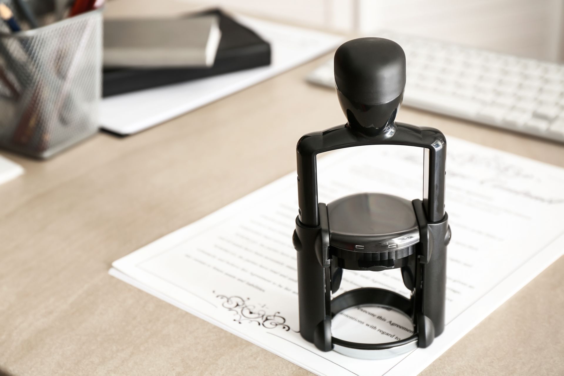 Black stamp on a stack of papers, near a keyboard and office supplies on a light wood desk.