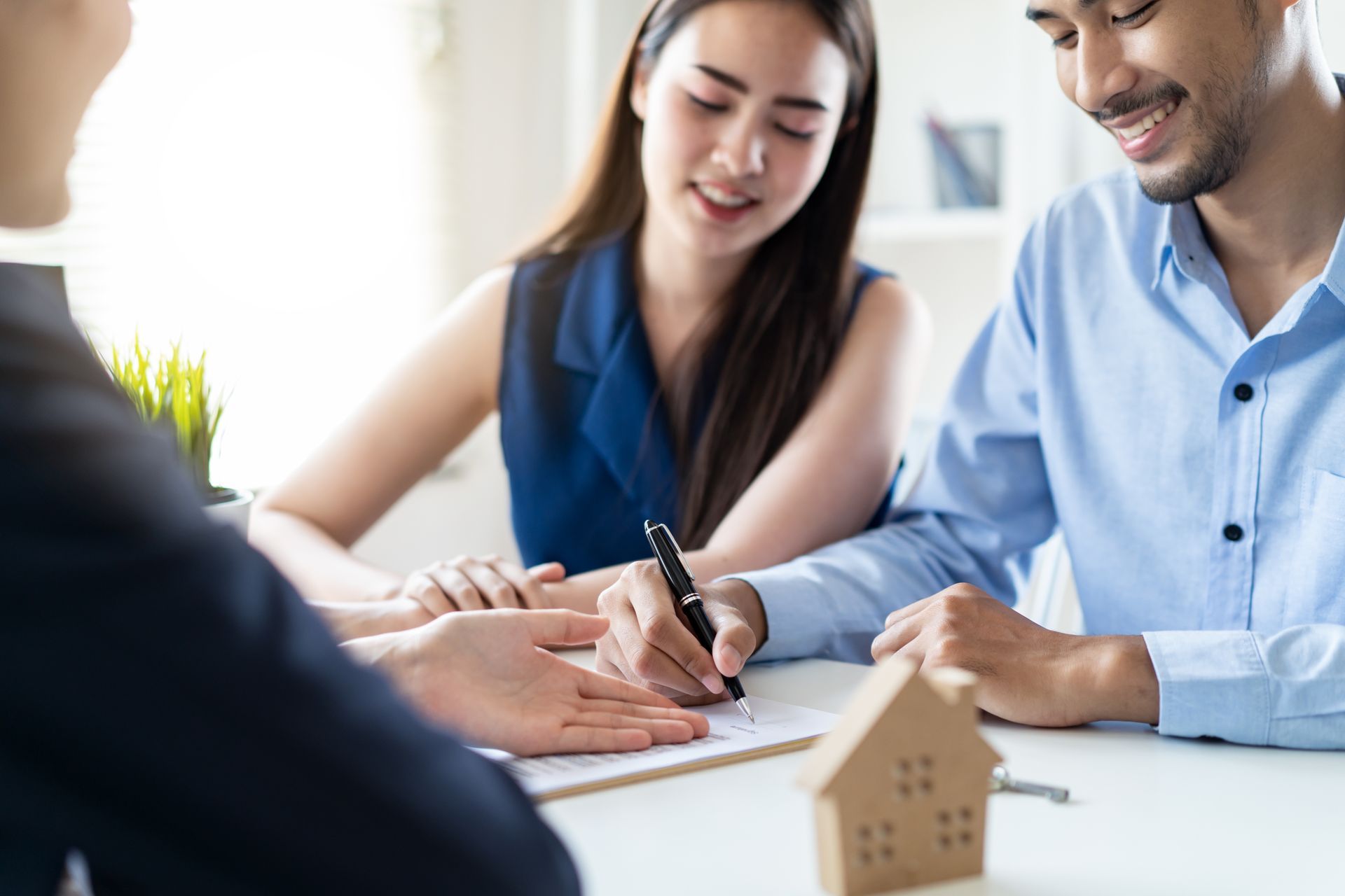 Couple signing paperwork with a realtor, small house model on the table.