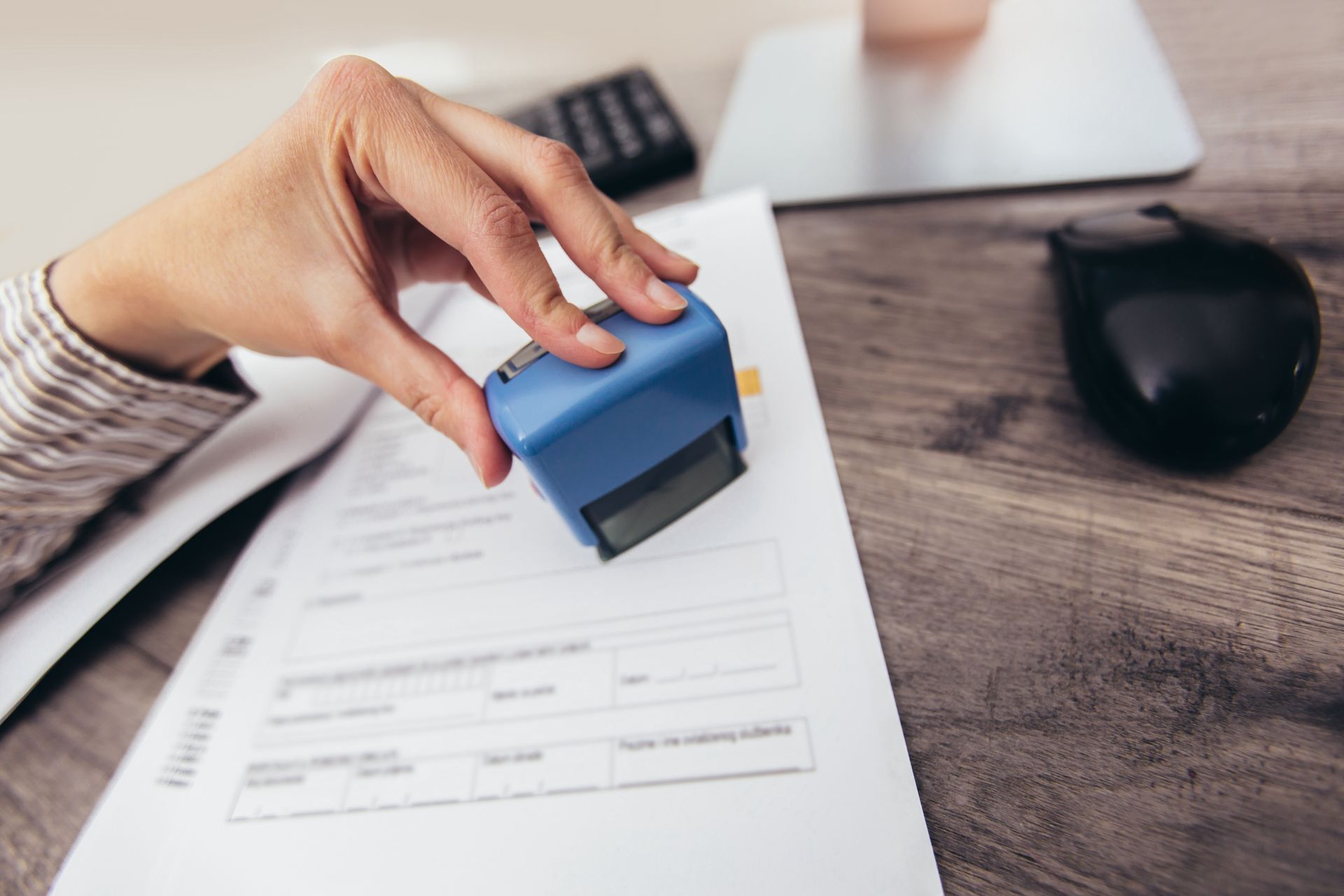 Hand stamping a document with a blue stamp on a wooden desk.