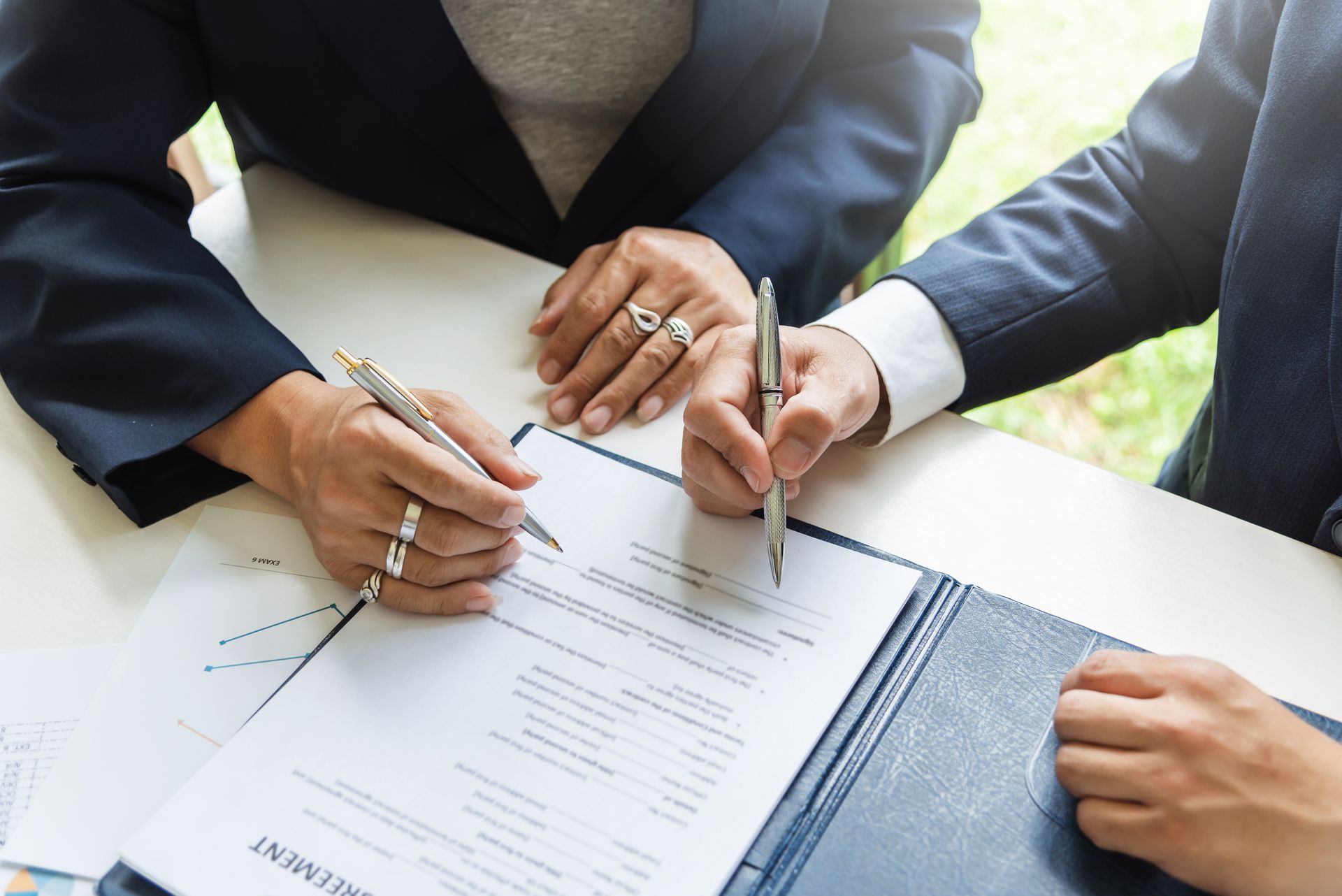 Two people signing a document at a desk, with pens in hand.