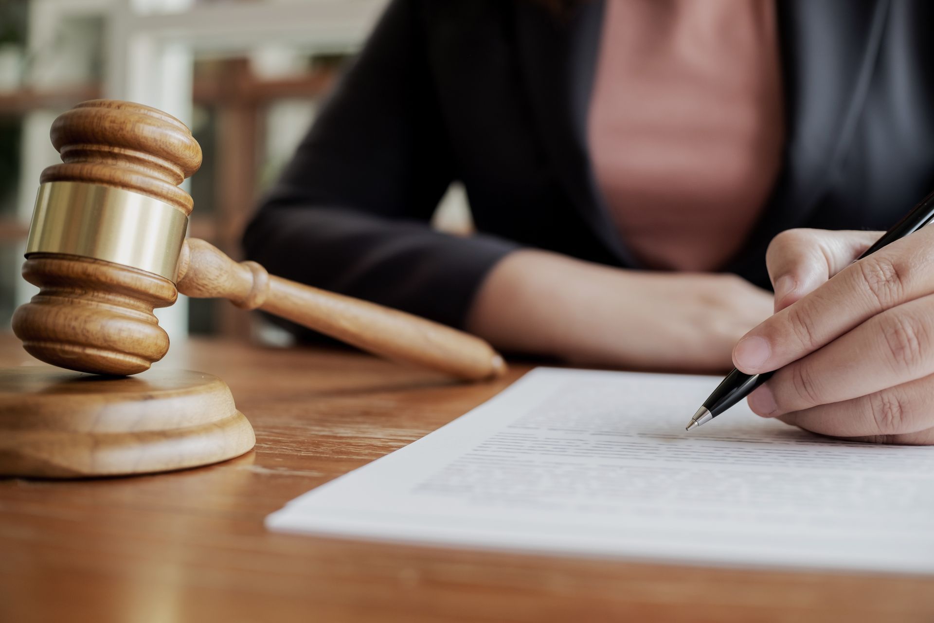 Gavel next to a person signing a document with a pen at a wooden table.