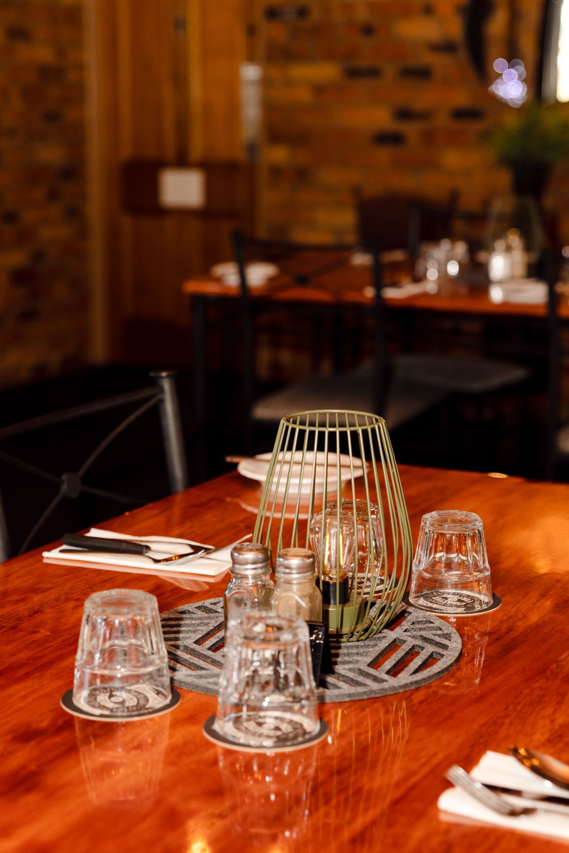 A wooden table with glasses and a lantern on it in a restaurant.