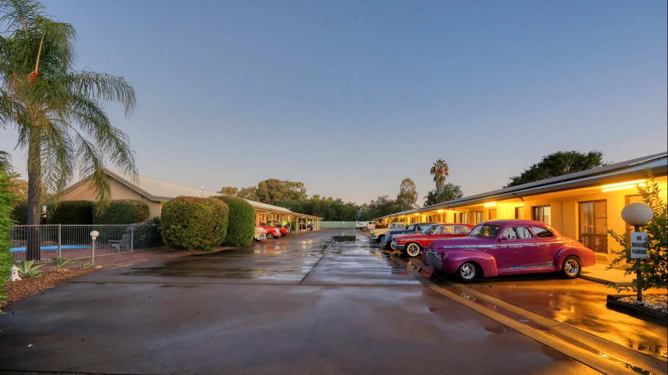 A row of cars are parked in front of a motel.