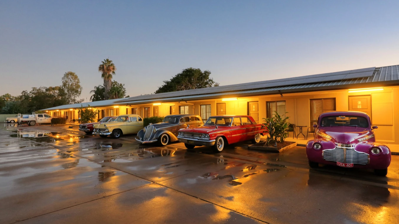 A row of old cars are parked in front of a motel.