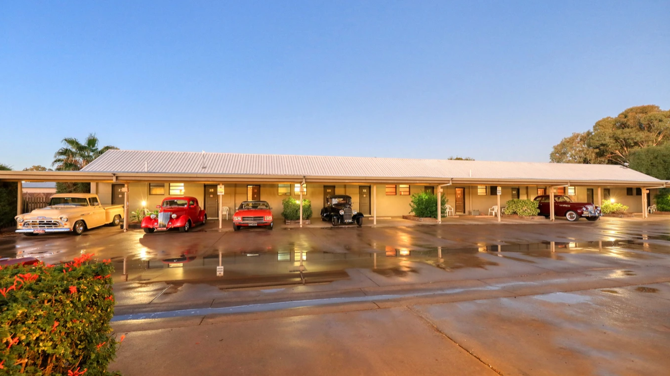 A motel with a lot of cars parked in front of it.