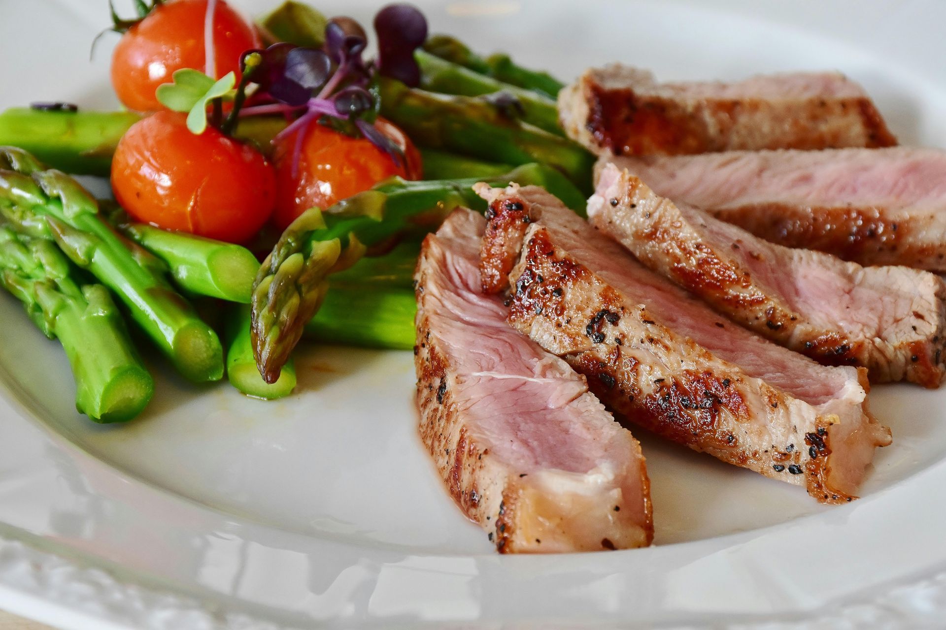 A white plate topped with meat , asparagus and tomatoes.