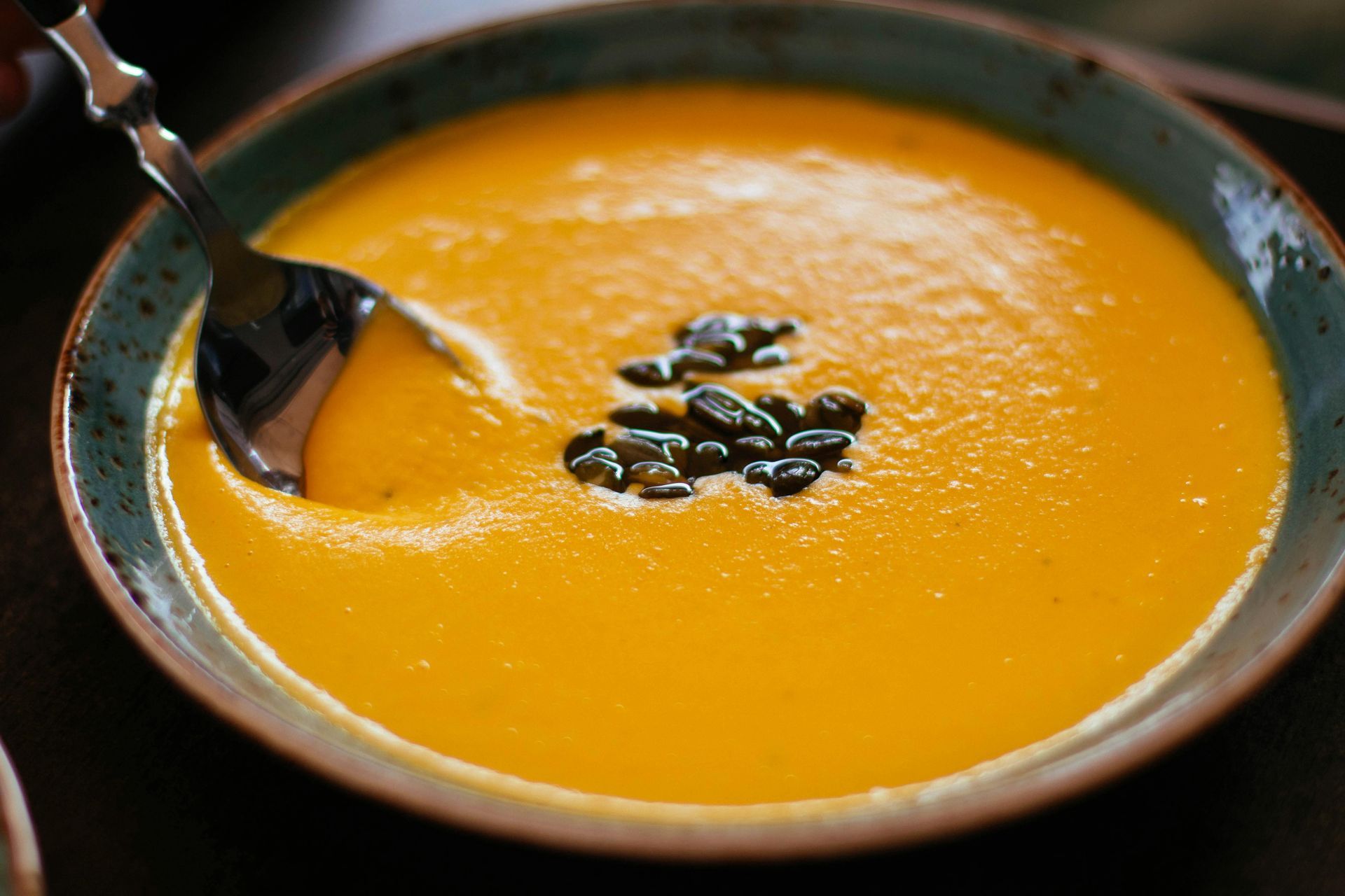 A bowl of soup with a spoon in it and pumpkin seeds on top.